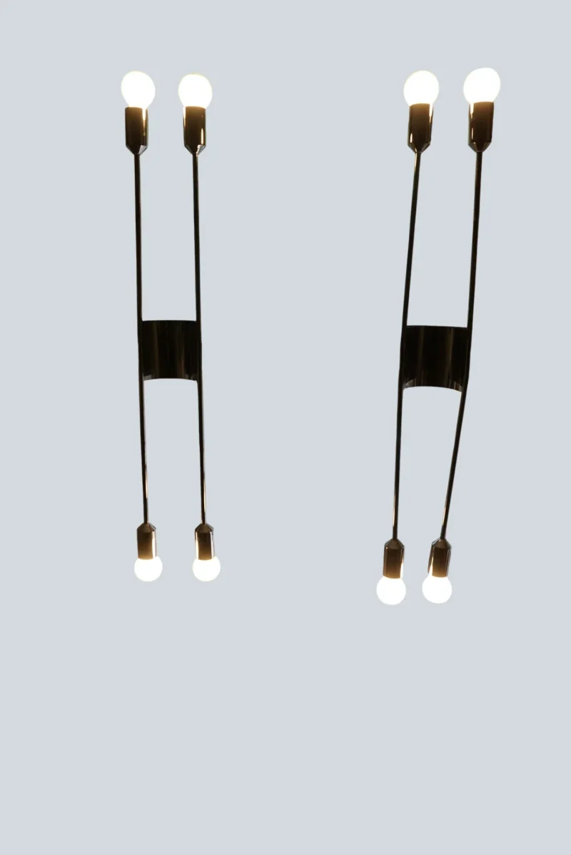 Front view of two illuminated Cosack 4166 wall sconces, showing the curved chrome connector and four glowing bulbs