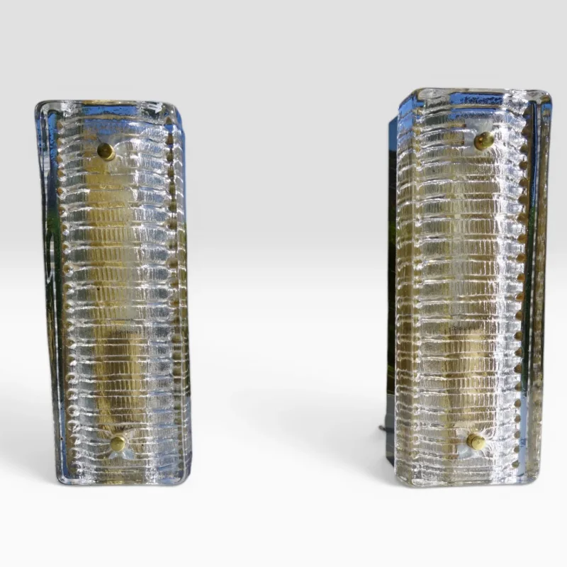 Paar Hillebrand Wandleuchten Modell 8971, strukturiertes Murano Eisglas mit charakteristischer Rippentextur und originalen Messingbolzen, Deutschland 1970er Jahre, Gesamtansicht beide Leuchten schräg  Nächstes Bild!  studioshot_portrait_cyclo-17.jpeg 11:52 Titel: Hillebrand Wandleuchten Paar Modell 8971 – Gesamtansicht frontal eingeschaltet  Alt: Paar Hillebrand Wandleuchten Modell 8971 eingeschaltet, warmes Licht durch strukturiertes Murano Eisglas, Gesamtansicht frontal symmetrisch, Messingbolzen sichtbar, Deutschland 1970er Jahre  Nächstes Bild!  studioshot_square_cyclo-26.jpeg 11:53 Titel: Hillebrand Wandleuchten Paar Modell 8971 – Ansicht von vorne mit Messingrückwand und Kabel  Alt: Paar Hillebrand Wandleuchten Modell 8971 von vorne, sichtbare originale Messingrückwand und Anschlusskabel, strukturiertes Murano Eisglas, Deutschland 1970er Jahre  Nächstes Bild!  studioshot_square_cyclo-27.jpeg 11:54 Titel: Hillebrand Wandleuchten Paar Modell 8971 – Rückansicht Wandhalterung und Befestigung  Alt: Rückansicht beider Hillebrand Wandleuchten Modell 8971, originale dunkelgrüne Metallrückwand mit Wandbefestigungsschlitzen und Anschlusskabeln, Deutschland 1970er Jahre  Nächstes Bild!