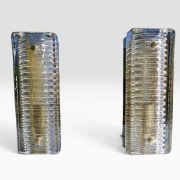 Paar Hillebrand Wandleuchten Modell 8971, strukturiertes Murano Eisglas mit charakteristischer Rippentextur und originalen Messingbolzen, Deutschland 1970er Jahre, Gesamtansicht beide Leuchten schräg  Nächstes Bild!  studioshot_portrait_cyclo-17.jpeg 11:52 Titel: Hillebrand Wandleuchten Paar Modell 8971 – Gesamtansicht frontal eingeschaltet  Alt: Paar Hillebrand Wandleuchten Modell 8971 eingeschaltet, warmes Licht durch strukturiertes Murano Eisglas, Gesamtansicht frontal symmetrisch, Messingbolzen sichtbar, Deutschland 1970er Jahre  Nächstes Bild!  studioshot_square_cyclo-26.jpeg 11:53 Titel: Hillebrand Wandleuchten Paar Modell 8971 – Ansicht von vorne mit Messingrückwand und Kabel  Alt: Paar Hillebrand Wandleuchten Modell 8971 von vorne, sichtbare originale Messingrückwand und Anschlusskabel, strukturiertes Murano Eisglas, Deutschland 1970er Jahre  Nächstes Bild!  studioshot_square_cyclo-27.jpeg 11:54 Titel: Hillebrand Wandleuchten Paar Modell 8971 – Rückansicht Wandhalterung und Befestigung  Alt: Rückansicht beider Hillebrand Wandleuchten Modell 8971, originale dunkelgrüne Metallrückwand mit Wandbefestigungsschlitzen und Anschlusskabeln, Deutschland 1970er Jahre  Nächstes Bild!